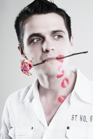 Red kisses on face of young man with rose at white backgroundの写真素材