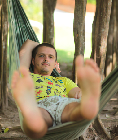 A handsome young man in yellow t-shirt resting in a hammock in the shade