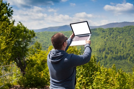 The man is trying to catch a connection with his laptop on the background of nature.