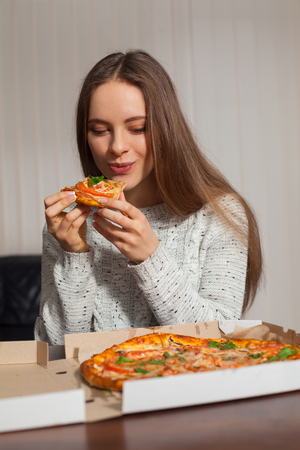 Beautiful young woman is eating pizza in the officeの写真素材