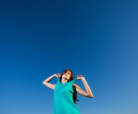 Pretty woman pulls straps of her blue dress against the blue skyの写真素材