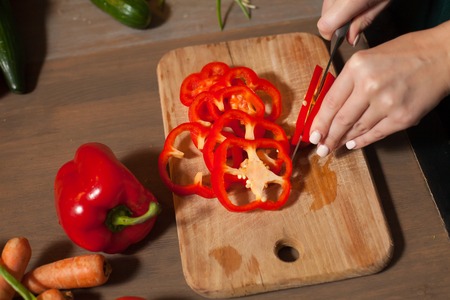 Woman is cutting a red pepper into rings at the tableの写真素材