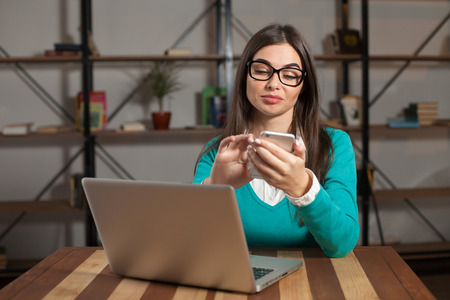 Freelancer is working with something and sitting at the wood table with drey laptop and  phone