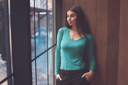 Beautiful woman is standing near the window and looks though it