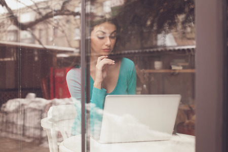 Through glass beautiful woman is working with laptop