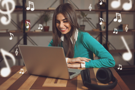 Smilling woman with  black headphones is sitting at the wood table with  laptop on the tableの写真素材