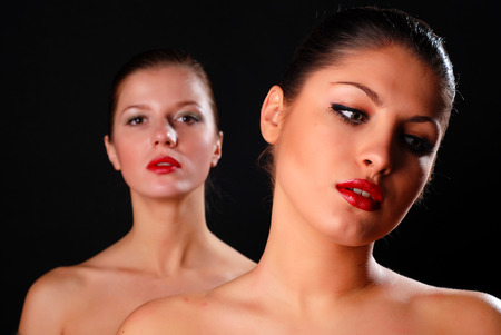 Two beautiful women at black background with red lipsの写真素材
