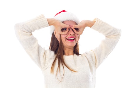 Young pretty woman in white sweater with red christmas hat making glasses with her hands on white background in studioの写真素材