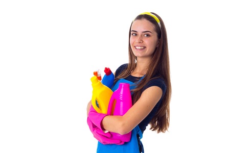Young positive woman in blue T-shirt and apron with pink gloves holding detergents on white background in studioの写真素材