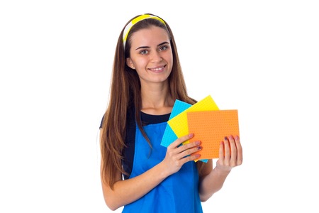 Young smiling woman in blue T-shirt and apron holding dusters on white background in studioの写真素材