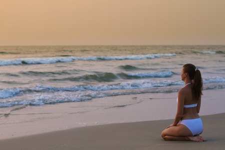 Young woman in white swimwear sitting on the sunset beachの写真素材