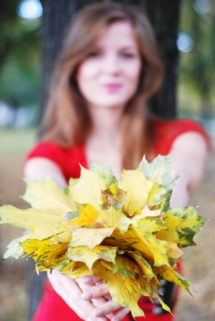 young happy beautiful woman in red with yellow maple leavesの写真素材
