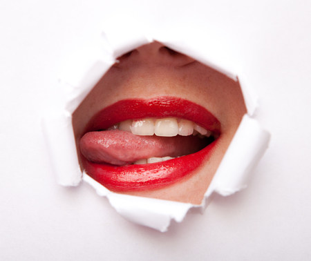 Lips of young beauty woman with red lipstick from paper holeの写真素材