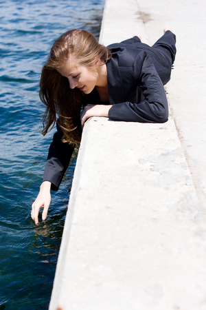 woman in black suit lying on the border near the waterの写真素材