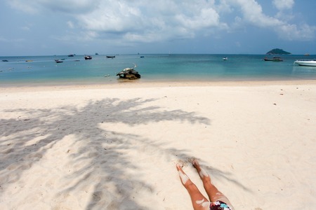 Young woman in a swimsuit lying on the sand at the beach. View from the back and shadow of palm treesの写真素材