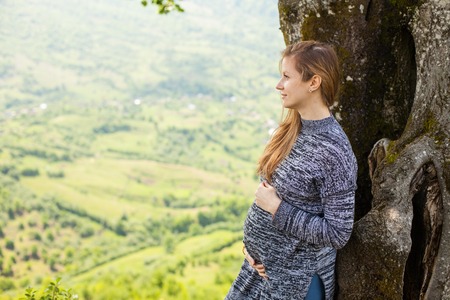 Pregnant woman is having a rest in the shade of a tree on the background of nature.の写真素材