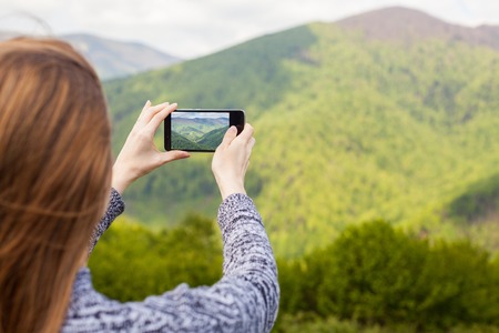 Beautiful young woman with long hair is doing a photo on her black phone of green nature.の写真素材
