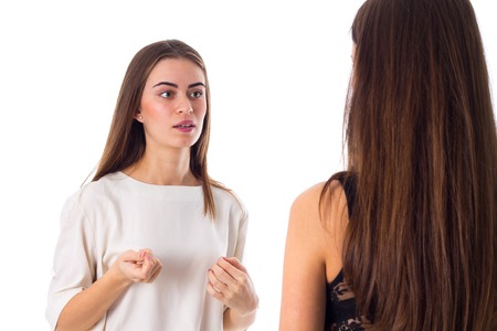 Young attractive woman in white shirt talking to another one on white background in studio