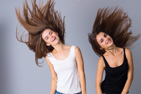 Two young charming women in black and white shirts jumping on gray background in studioの写真素材