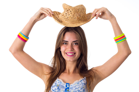 Young pretty woman in blue T-shirt with colored bracelets smiling and holding her hat up on white background in studioの写真素材