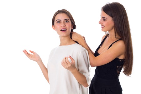 CHarming young woman in black shirt making another talking woman in white shirt a plait on white background in studioの写真素材