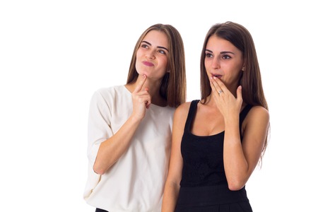 Two attractive young women in black and white shirts looking on something and thinking on white background in studioの写真素材