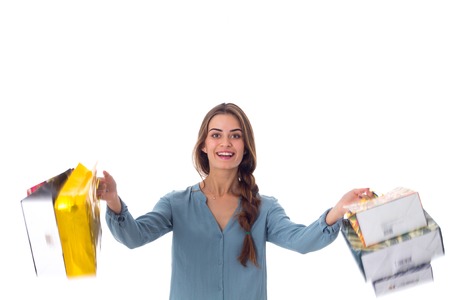 Young pleasant woman in blue blouse holding varicolored shopping bags in her hands on white background in studioの写真素材