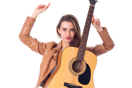 Pretty young woman in brown jacket with  guitar holding hands up on white background in studio