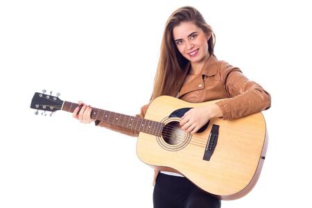 Young happy woman with long hair in brown jacket holding a guitar on white background in studio