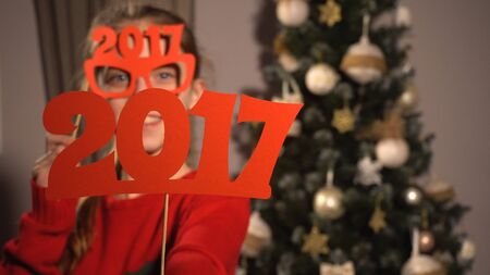 Pretty girl in red sweater holding red banners with figures 2017 on the background of christmas tree in the light roomの写真素材