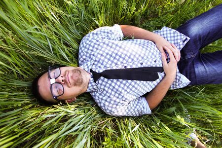 A handsome young man in glasses lying on green grass with eyes closedの写真素材
