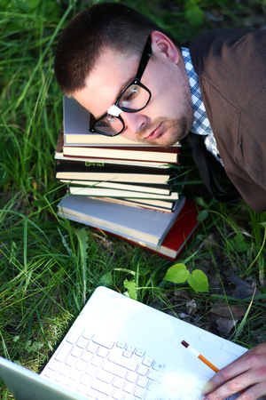 A man in glasses sleeping on the books on the grassの写真素材