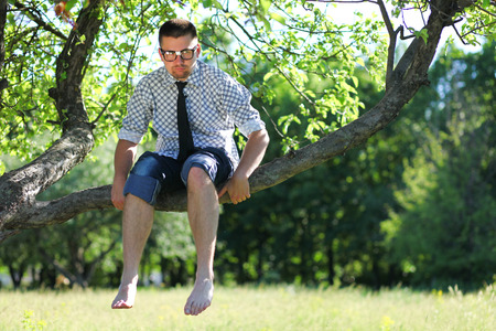 A serious man in glasses sitting barefoot on the branch of the treeの写真素材