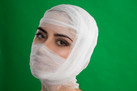 The woman with beautiful brown eyes and a bandage on her head is posing against the background of chromakey.の写真素材