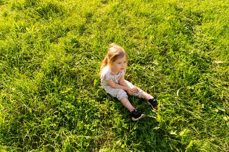 Little girl sitting on lawn in the summer sunny dayの写真素材