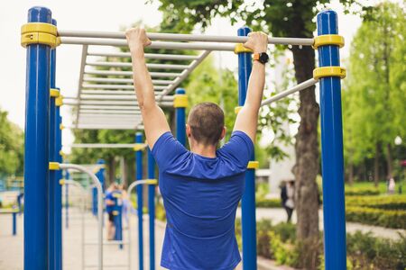 Man doing pull ups workout in the ground park. View from back.