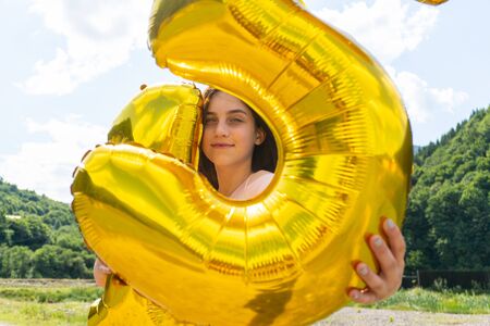 Teen girl looking through golden balloons in cameraの写真素材