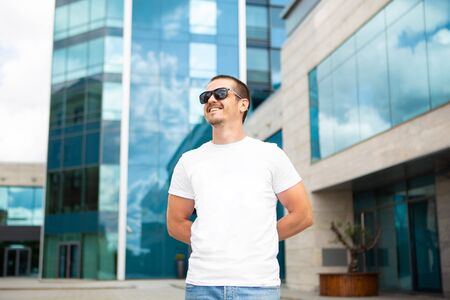 Adult man in white blank t-shirt standing near modern buildingの写真素材
