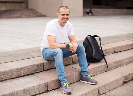 Man looking in camera and smiling while sitting on stairsの写真素材