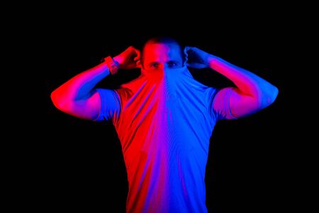 Man hiding his face under t-shirt, red and blue color lightの写真素材