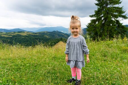Little smiling girl standing outdoor with mointains viewの写真素材