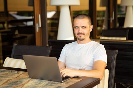 Man with laptop looking in camera while sitting in cafeの写真素材