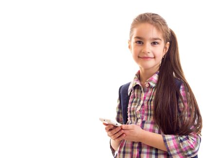 Positive schoolgirl looking in camera while holding smartphoneの写真素材