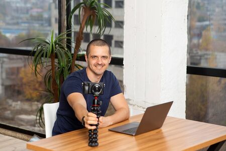 Man video blogger holding camera while sitting at the table with laptopの写真素材