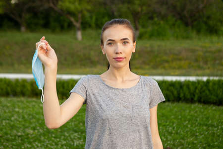Woman holding medical blue mask in her hand standing outdoors.の写真素材