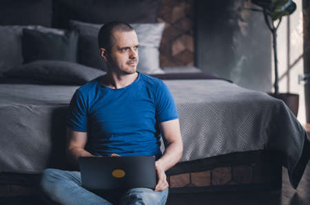 Adult man in blue t-shirt working on laptopの写真素材