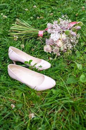 Wedding shoes and purple white and pink boho bouquet on green grass background. Beautiful bouquet of wild flowers and pump court shoe in pink. Vintage boho shot wedding decoration flowers. Poppy, garlic, rose flowers.の写真素材