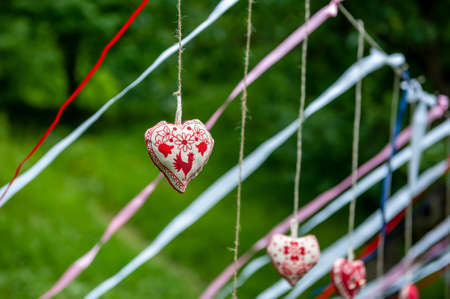 Four handmade cotton fabric heart in line with ribbons hanging on bast string on tree on green grass background. Red fabric heart hanging on the clothesline. Summer wedding theme. Love and valentine in nature.の写真素材