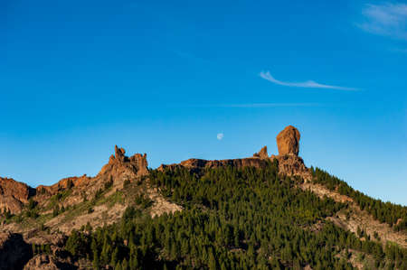 Roque Nublo, symbolic natural monument of Gran Canaria, Canary Islands. Summer sunny day with blue skies and moon and cloud sky. Emblematic volcanic rock formations in the mountains of Gran Canaria Spain.の写真素材