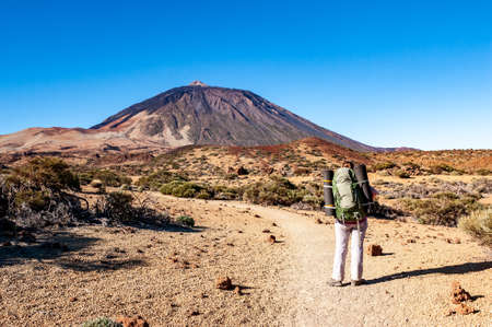 Young woman hiker with backpack looking at Pico del Teide mountain in El Teide National park. Tenerife, Canary Islands, Spainの写真素材
